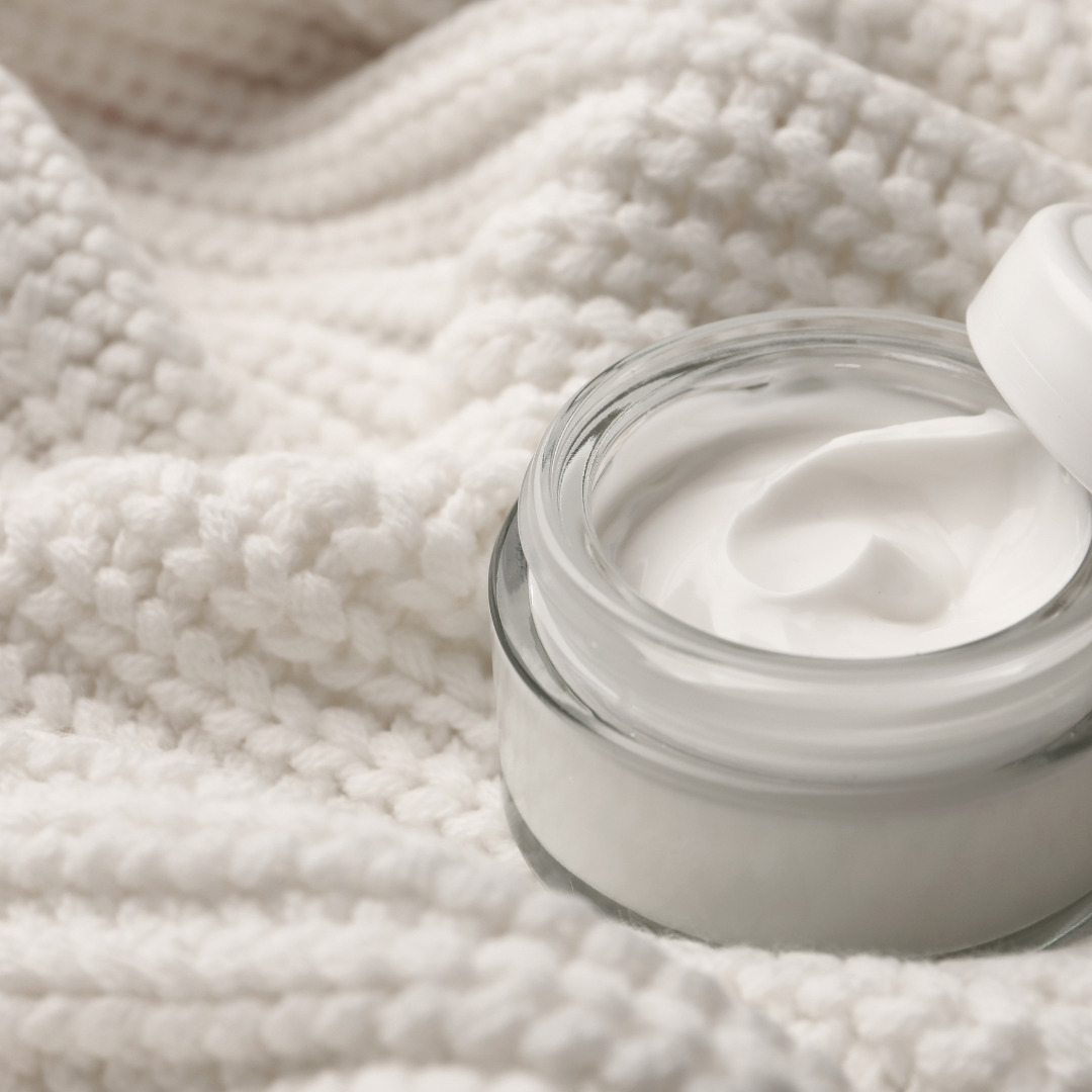 Jar of face cream on white wool sweater background.