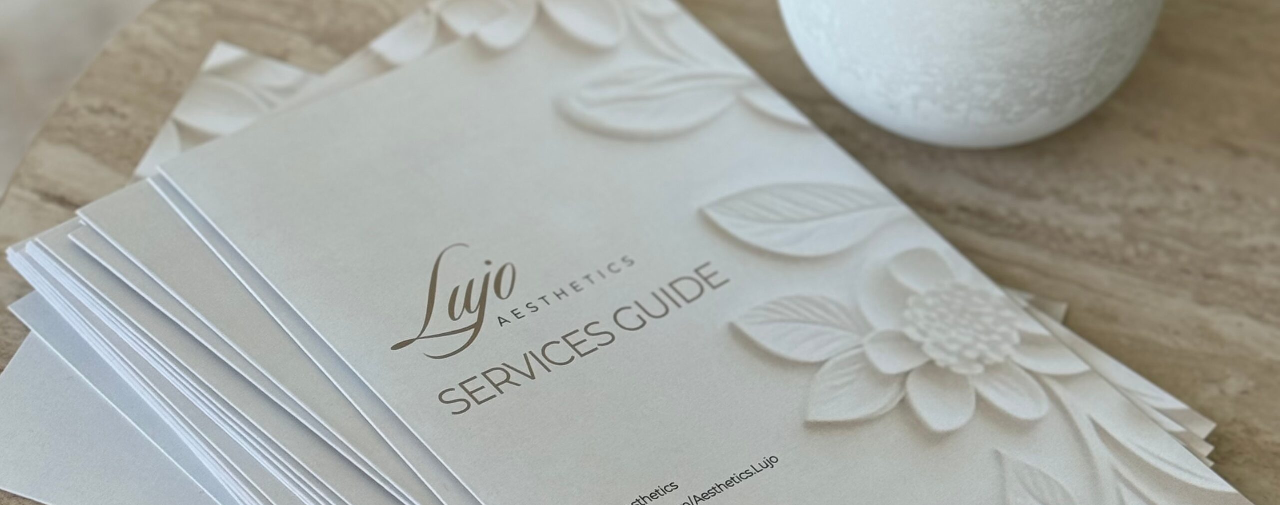 Table with Lujo Aesthetics service menus and a candle.